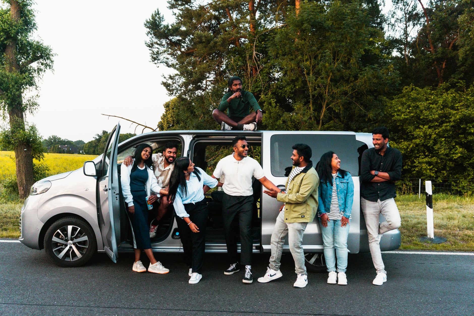 A group of friends having fun by a van on a scenic road trip in nature.